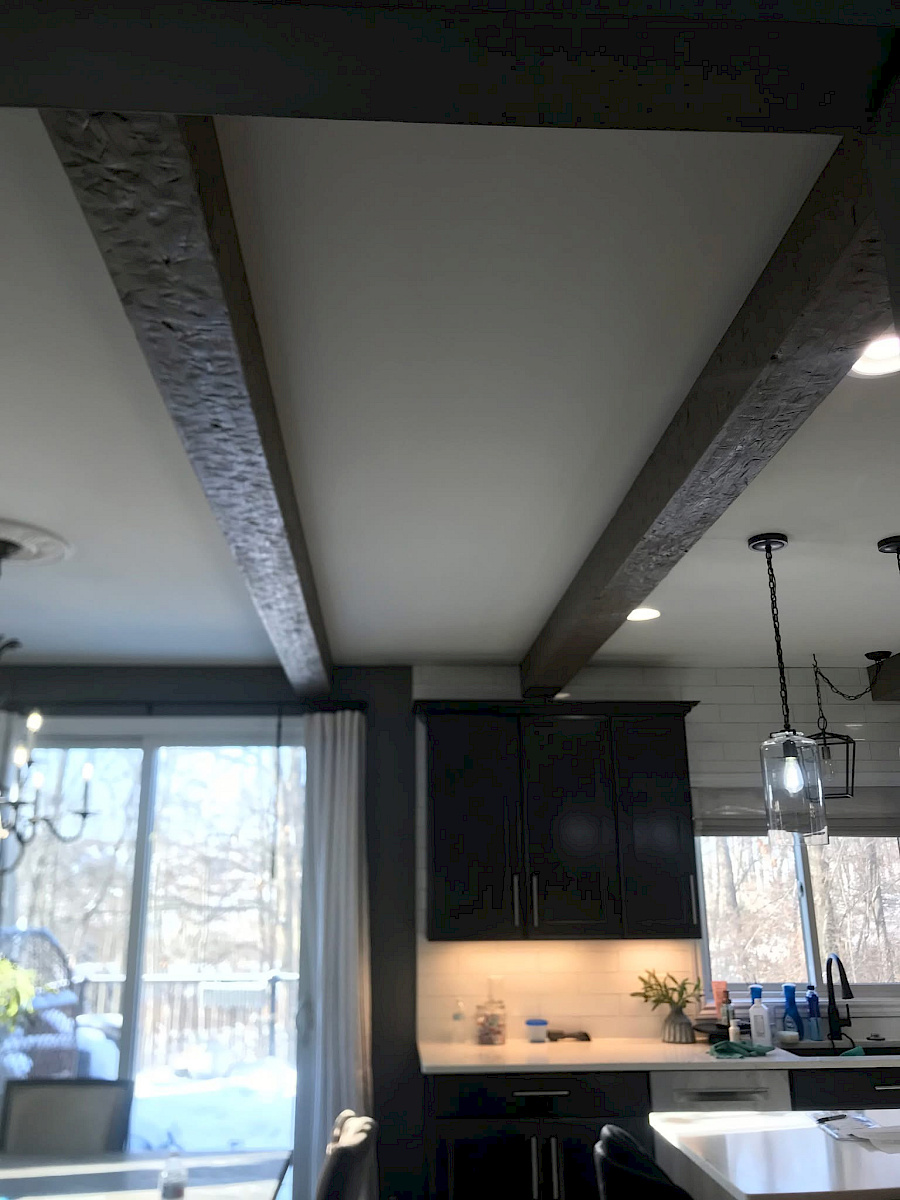 Remodeled kitchen with rustic hand-finished wood ceiling beams above dark cabinetry and a white subway-tile backsplash.