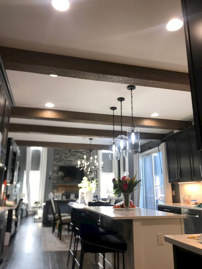 Open kitchen with a wood-beam ceiling, recessed and pendant lighting, a quartz island, and a sightline to a stone fireplace.