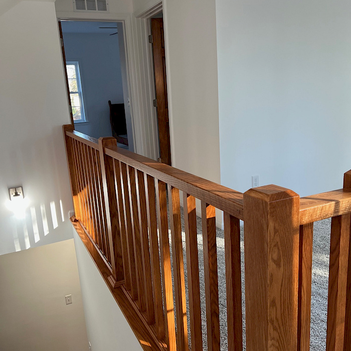 Open oak staircase with custom railing and balusters on a carpeted second-floor landing with a vaulted ceiling.