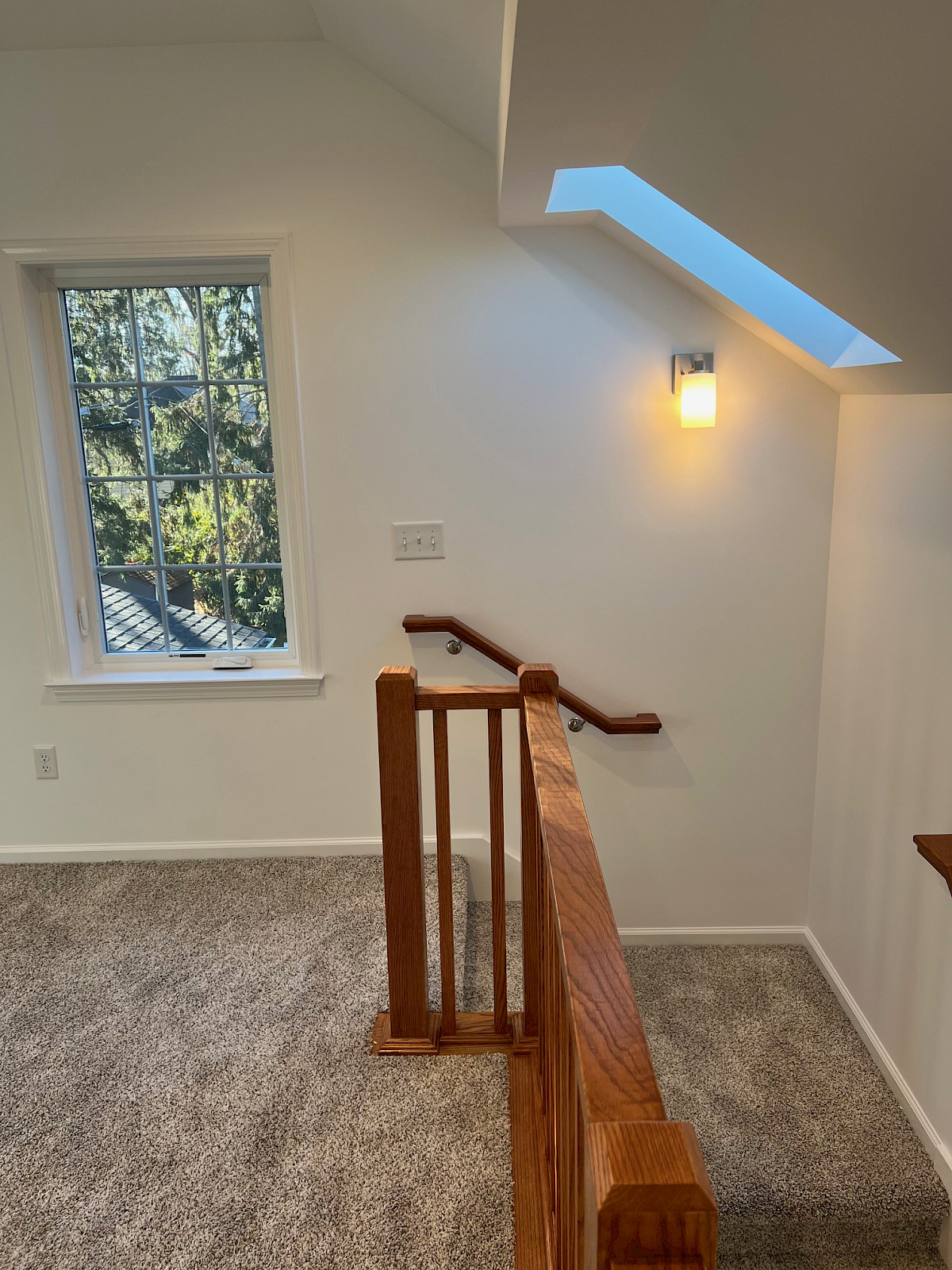 Second-story addition featuring a vaulted ceiling, skylight, oak stair railing, and a carpeted loft landing.