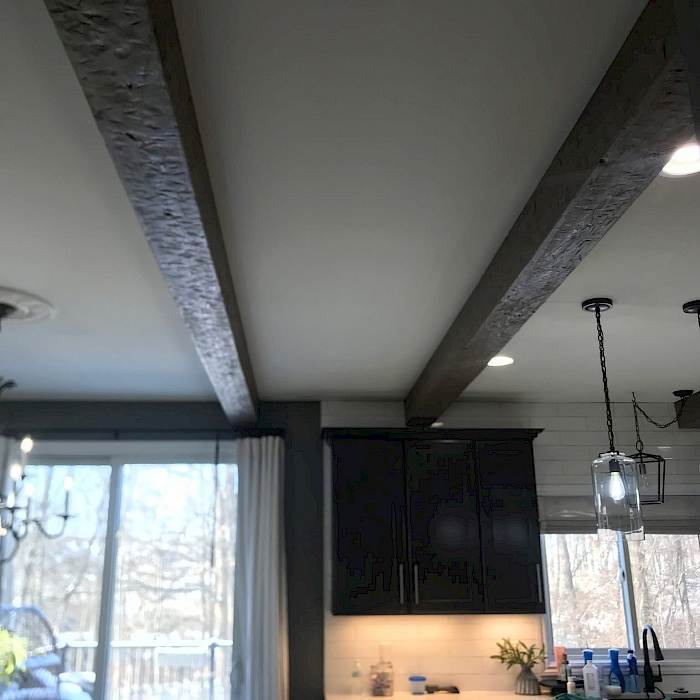 Remodeled kitchen with rustic hand-finished wood ceiling beams above dark cabinetry and a white subway-tile backsplash.