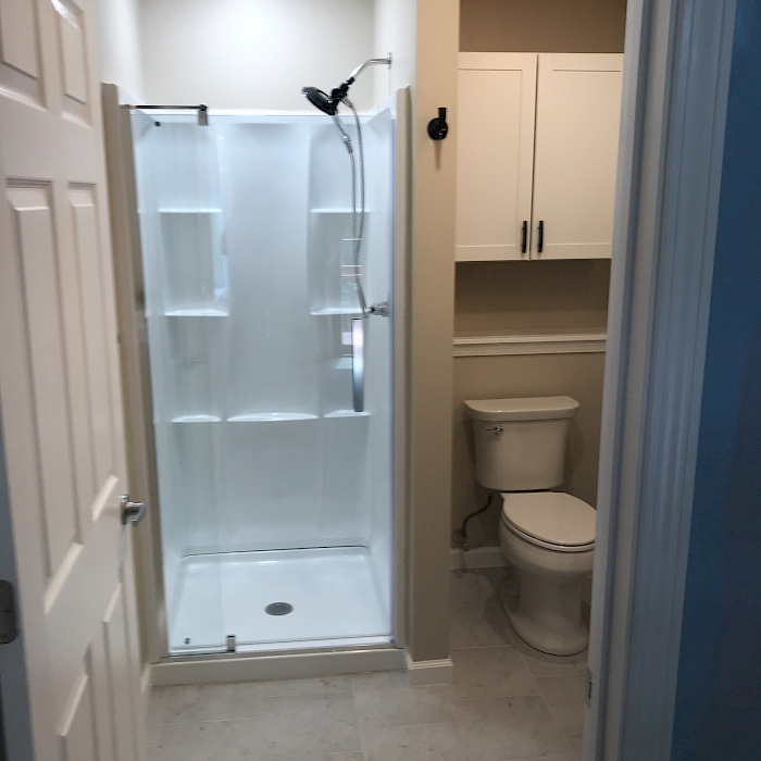 Remodeled bathroom with a white shower enclosure, glass door, tiled flooring, and a built-in storage cabinet above the toilet.