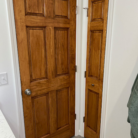 Custom-stained six-panel door beside a narrow paneled linen-closet door with bronze hardware.
