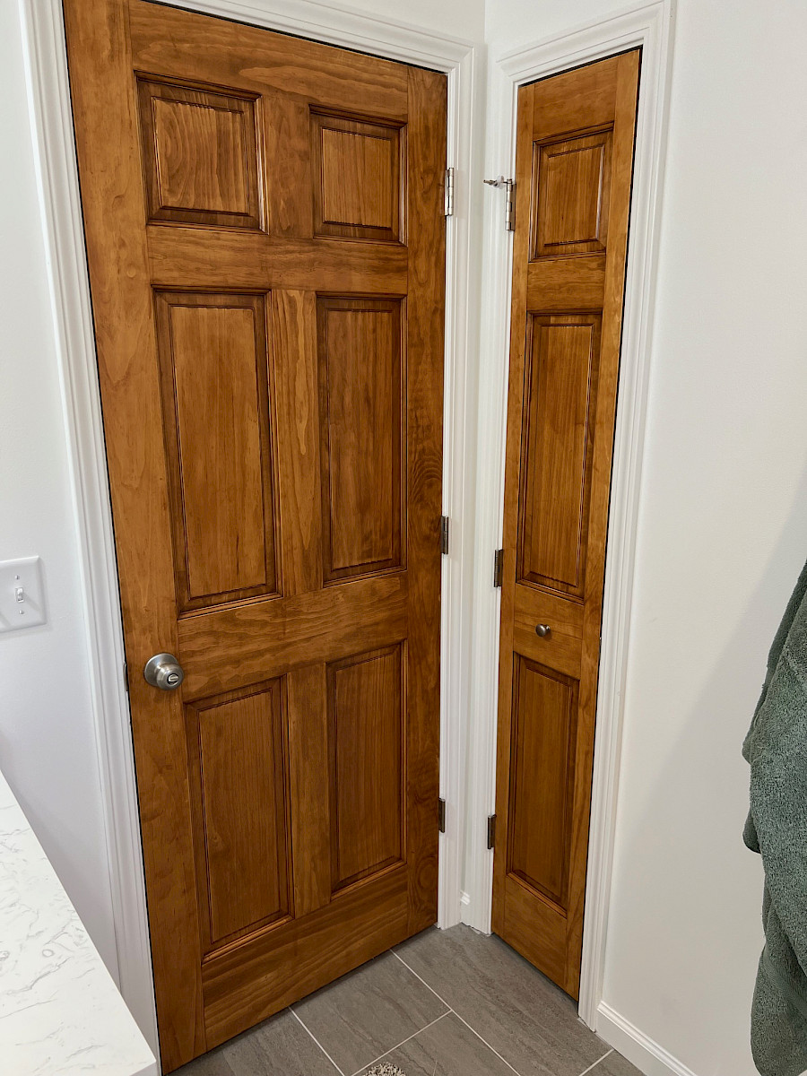 Custom-stained six-panel door beside a narrow paneled linen-closet door with bronze hardware.