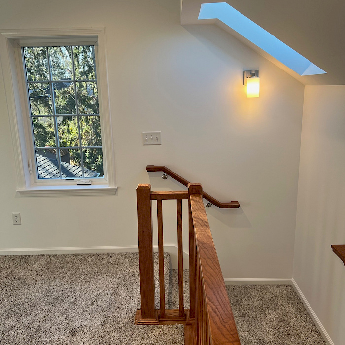 Second-story addition featuring a vaulted ceiling, skylight, oak stair railing, and a carpeted loft landing.