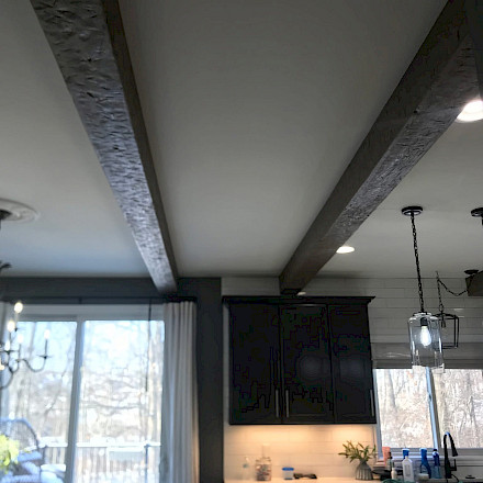 Remodeled kitchen with rustic hand-finished wood ceiling beams above dark cabinetry and a white subway-tile backsplash.